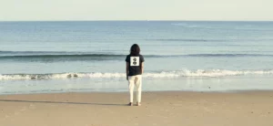 Homme de dos sur la plage de l'Uhabia à Bidart avec un tee shirt dessiné par l'artiste américain James Coffman pour Bask in the Sun